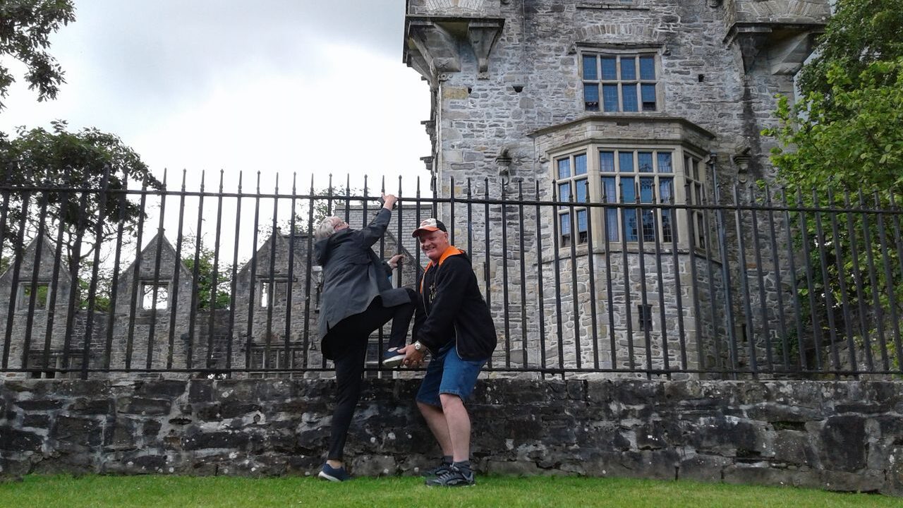 Two new friends by the outer barriers of a castle, pretending to give one another a leg up to scale the barrier.