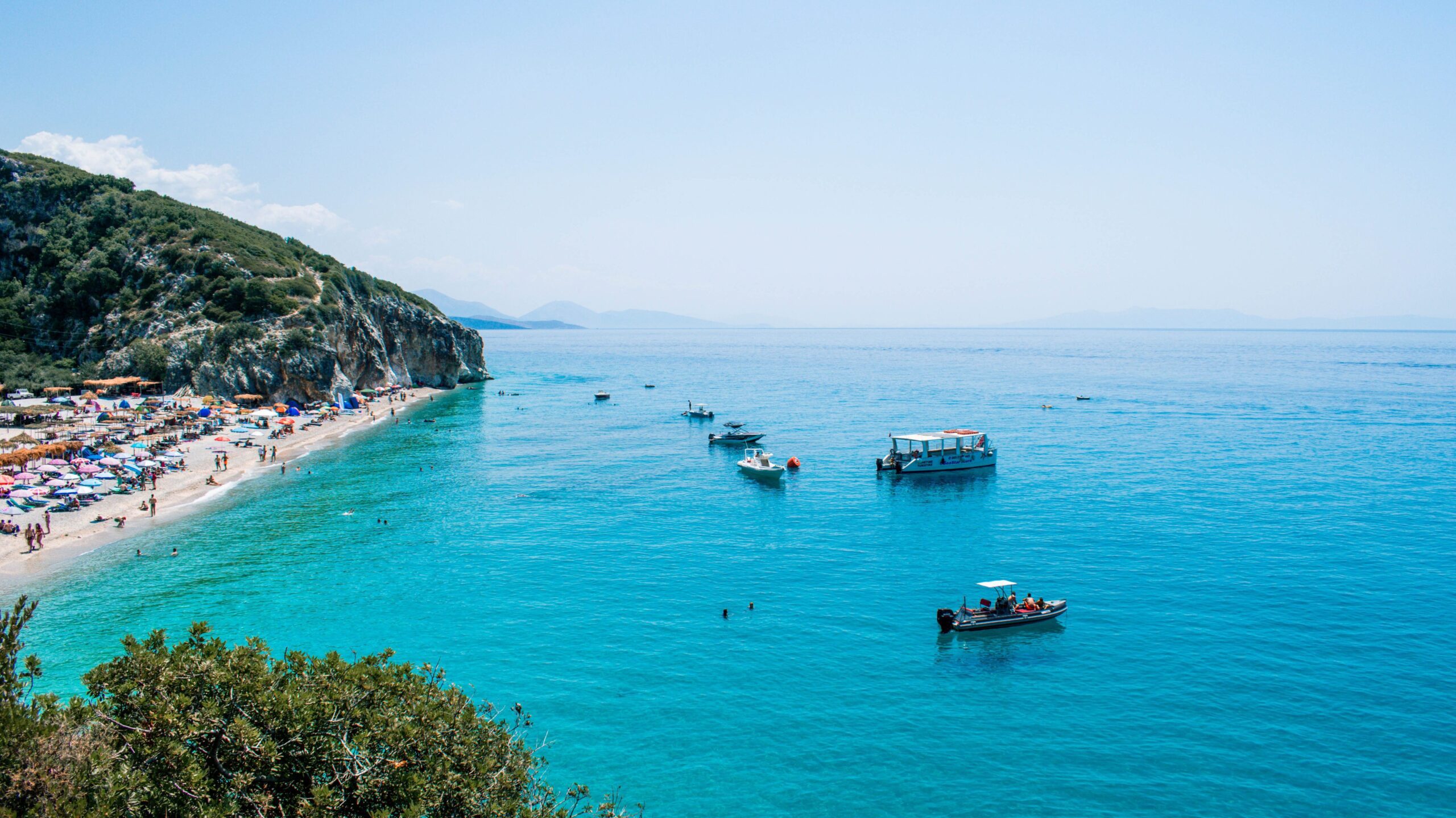 A wide angle view of Gipje Beach and a gorgeous expanse of azure waters on the right. Small boats float on the bay. This is one of the best Eastern Europe beaches