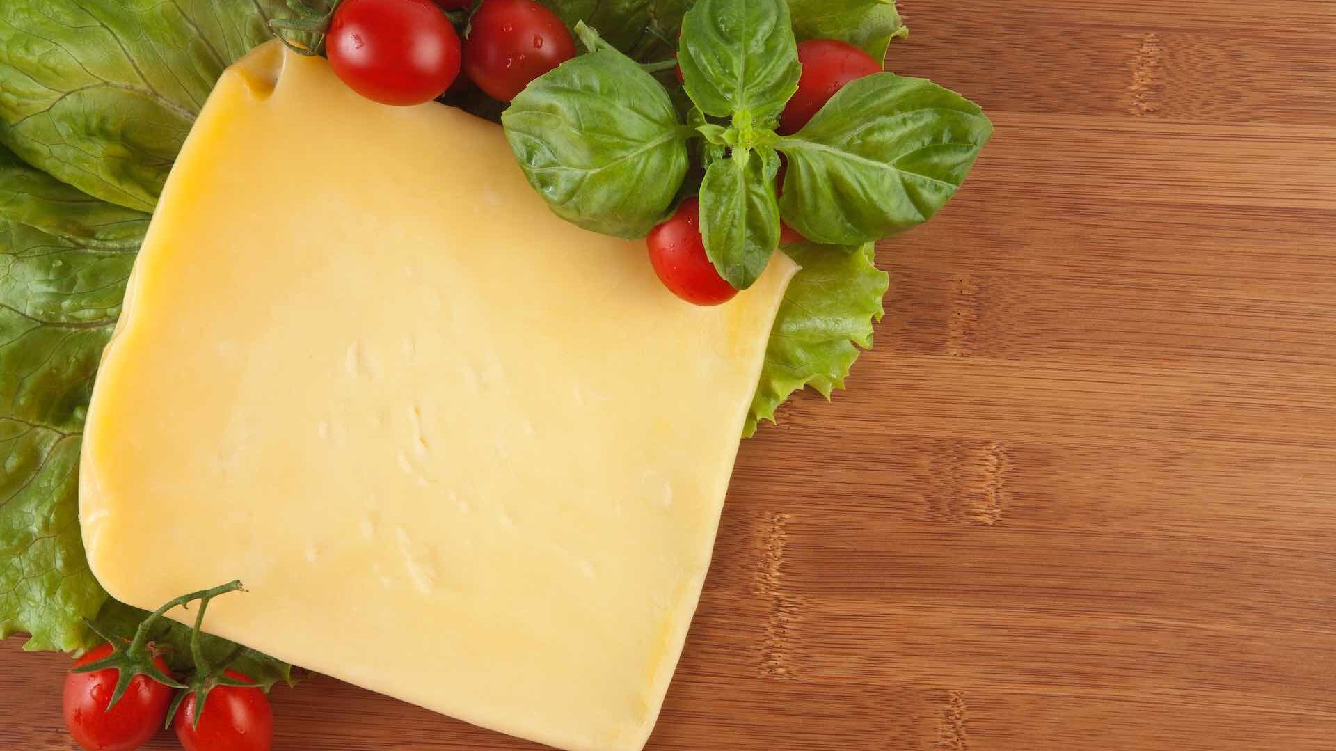 Birdseye view of a wedge of yellow cheese on a table with cherry tomatoes and lettuce