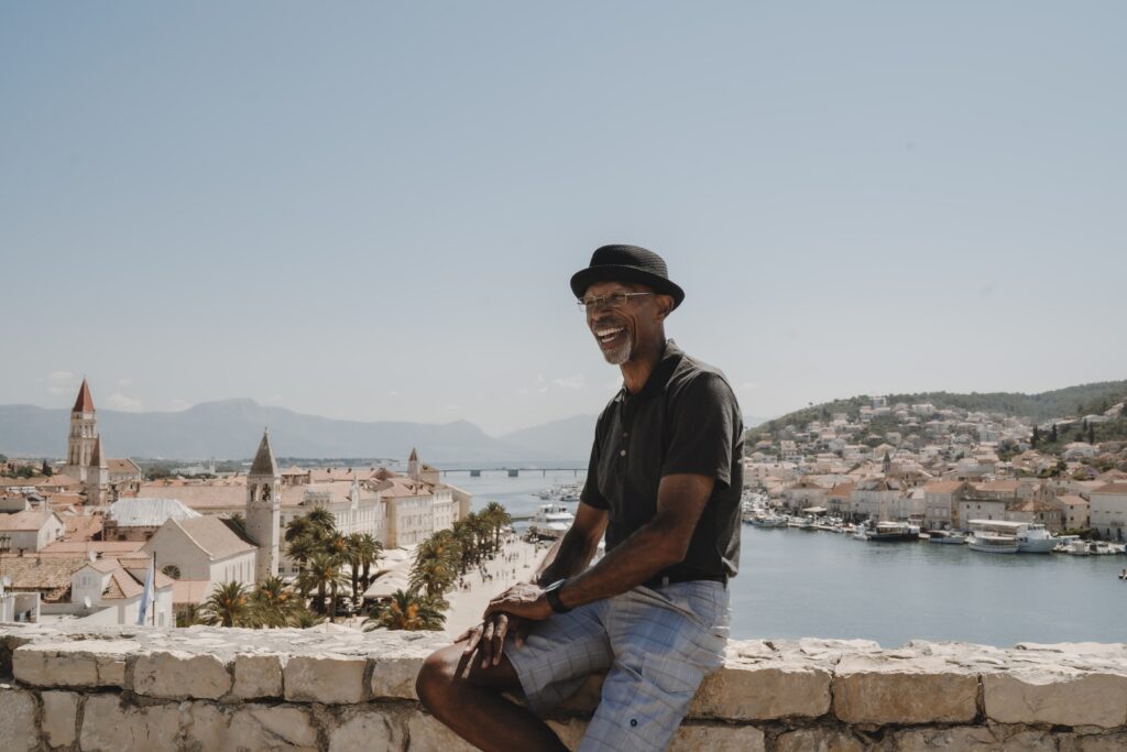 Lawrence smiling while posing on a wall, wearing a polo shirt and a black hat, enjoying his multigenerational travel tour