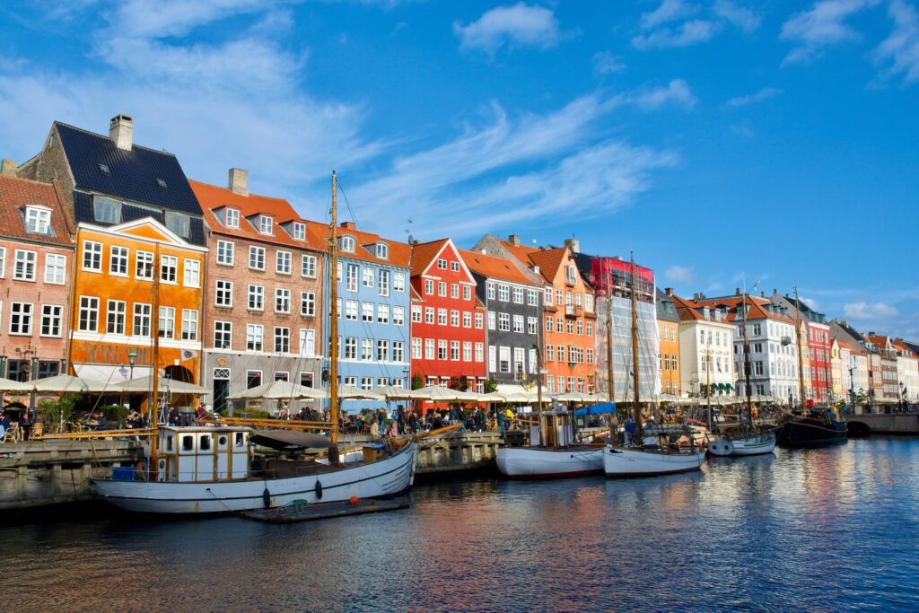 Brightly colored buildings line the waterfront at Nyhavn with boats moored in the canal, under a clear blue sky, making it a picturesque spot in family-friendly European cities.