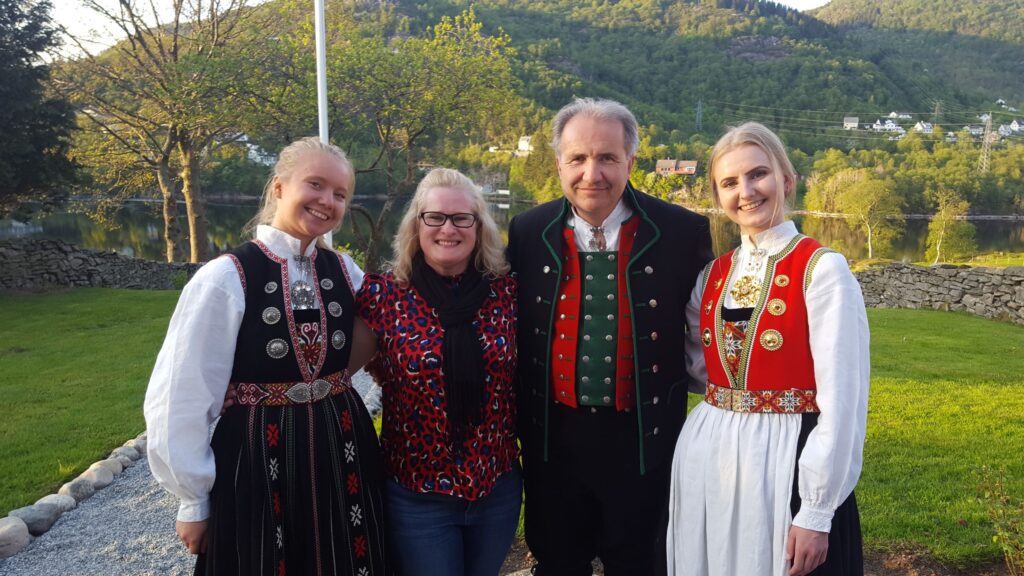 The Øvre-Eide family pose for a photo in a field, in traditional Norwegian garb. They can't wait to host more guests for their Be My Guest experience