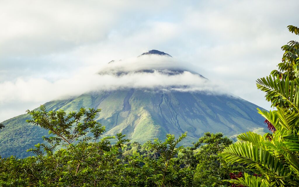 A volcano in Arenal, Costa Rica, towering up in the sky with a ring of clouds around it. Another beautiful landscape you'll see if you go to Costa Rica for Christmas