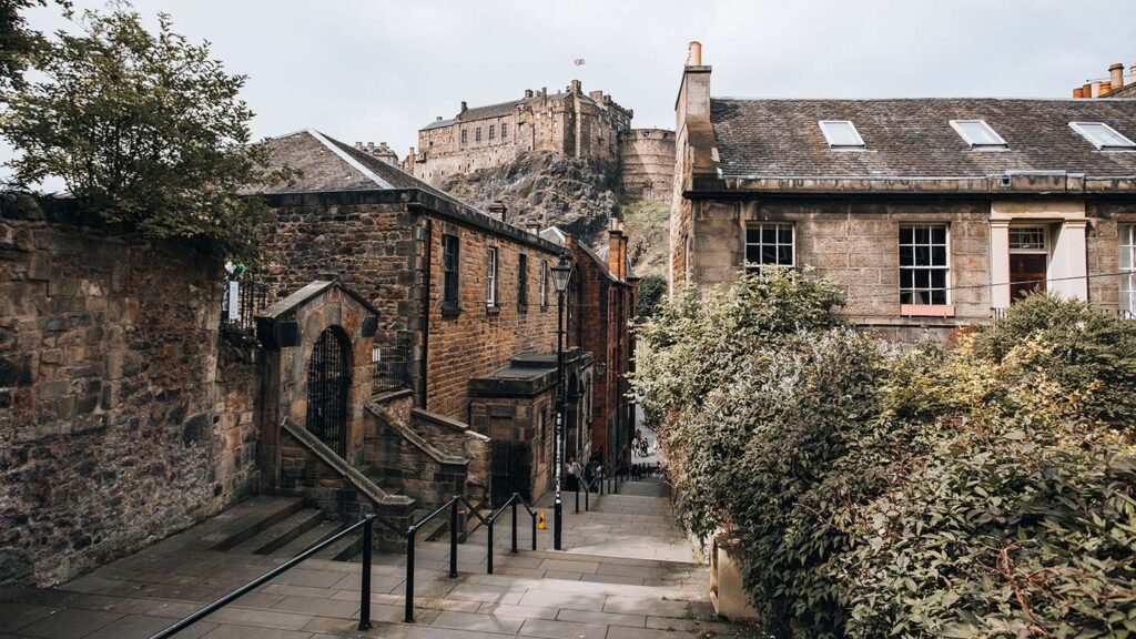 Stairs in the center, with houses and buildings on the side in Edinburgh, one of the best places to visit for Halloween. Can see the Edinburgh Castle in the background of the image on the hill