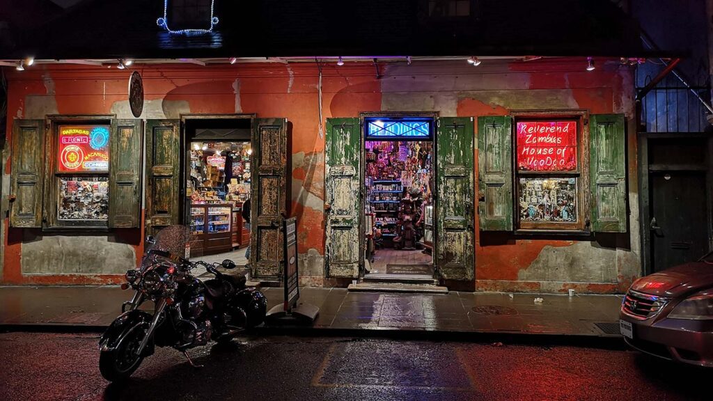 A store in New Orleans, with colorful lights inside and the shutter-style doors and windows are open. Motorbike outside.