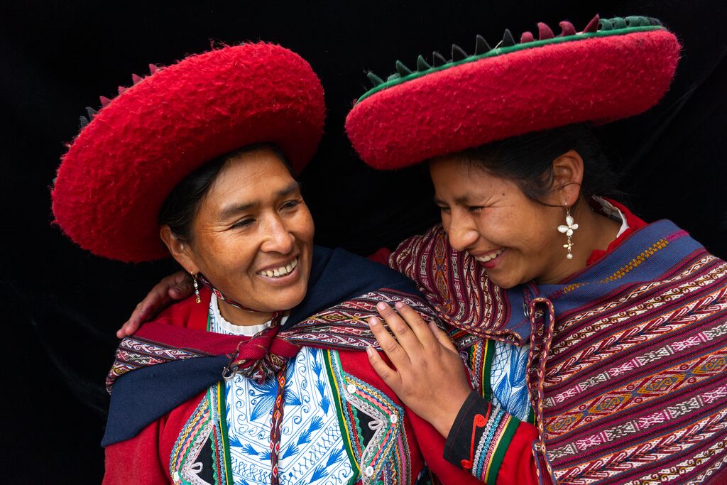 Two Peruvian women laughing and holding each other while in traditional dress.