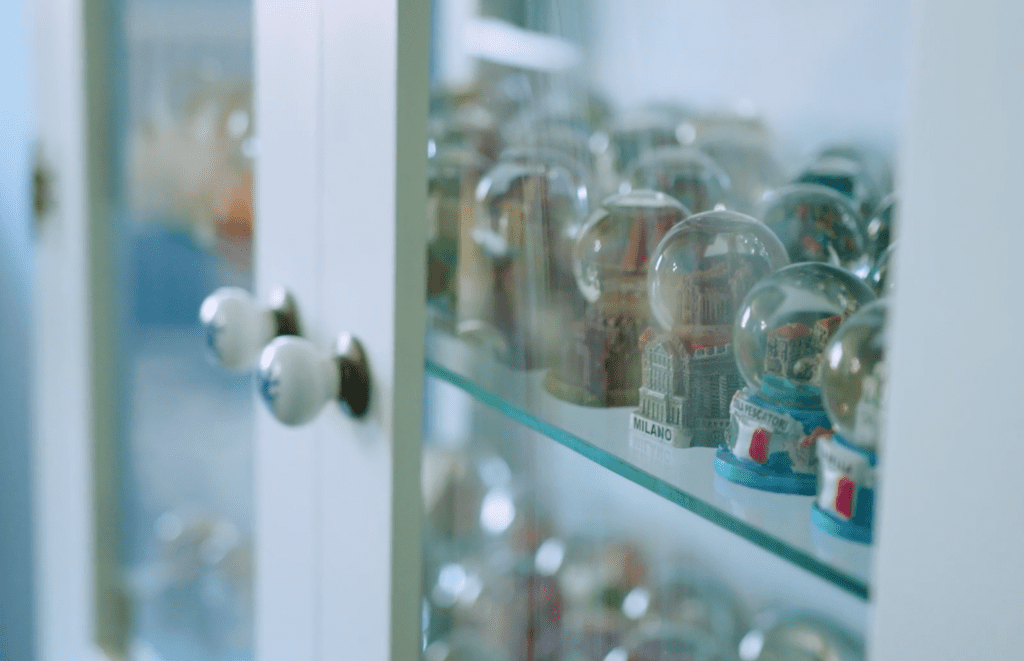 Numerous snow globes sit together in a white wood and glass fronted display cabinet