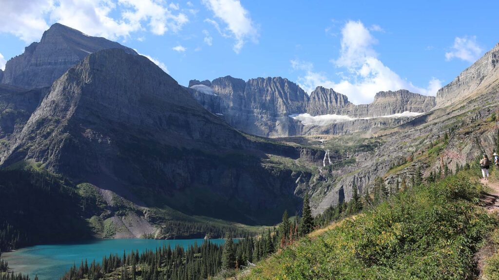 View looking across a blue glacial lake and hillside towards a mountain ridge in Glacier National Park