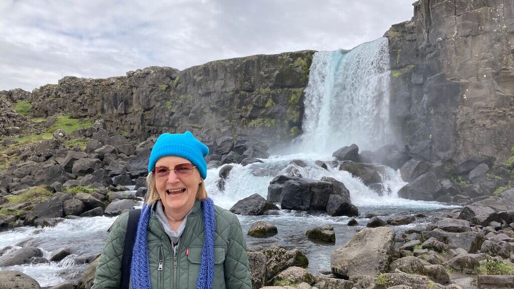 Past guest Elizabeth F. standing in front of a waterfall in Iceland