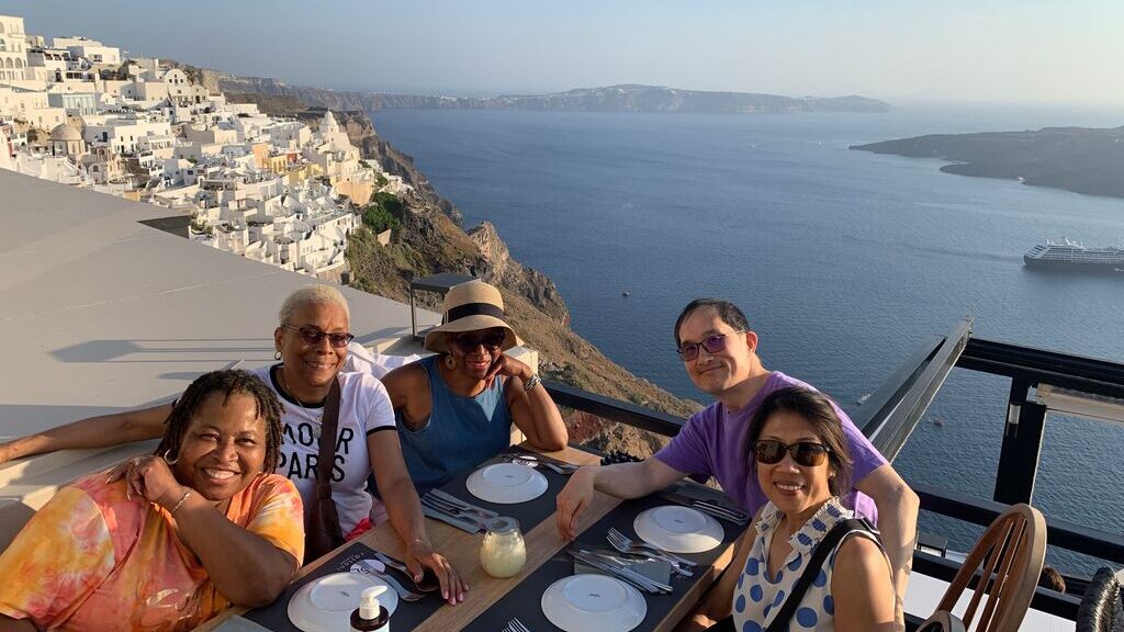 Past Trafalgar guest Li T. with fellow guests at a restaurant overlooking Santorini