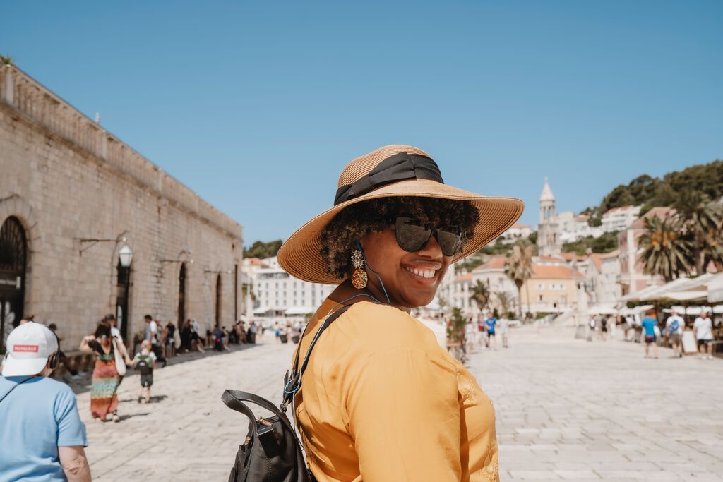 Portrait of a Trafalgar guest smiling over her shoulder at the camera, wearing a hat, sunglasses and a yellow top