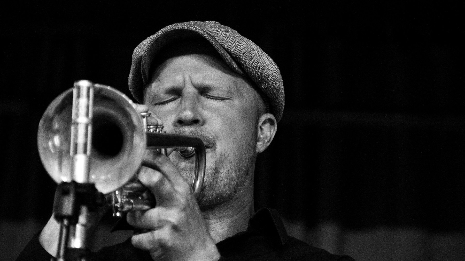 Black and white photo of a man wearing a tweed flat cap playing the trumpet