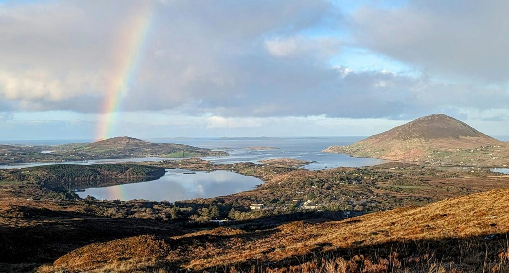 Photo of a rainbow over an Irish landscape view, with hills, sea and islands