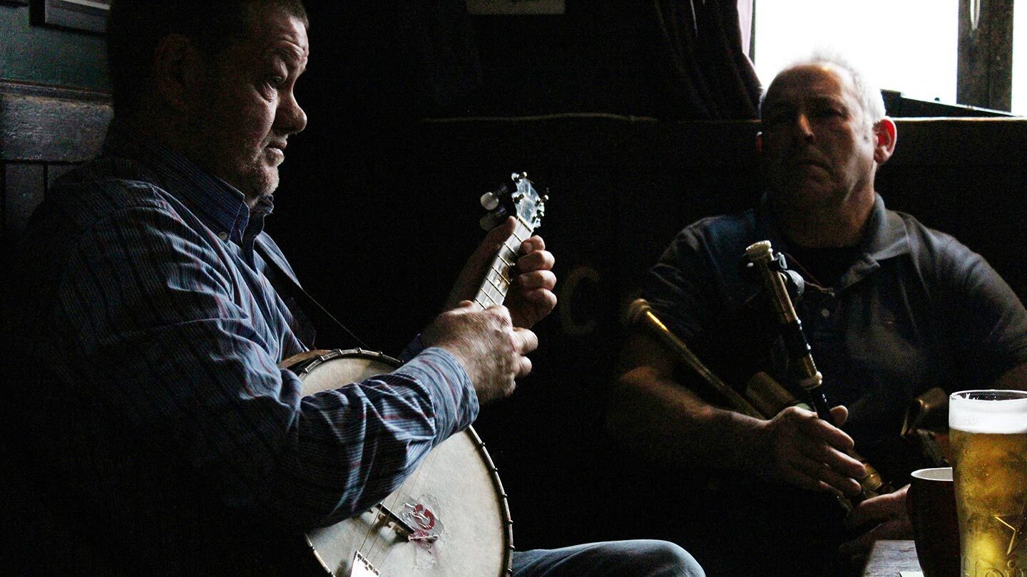 Two Irish musicians photographed with their instruments in a pub, in low light