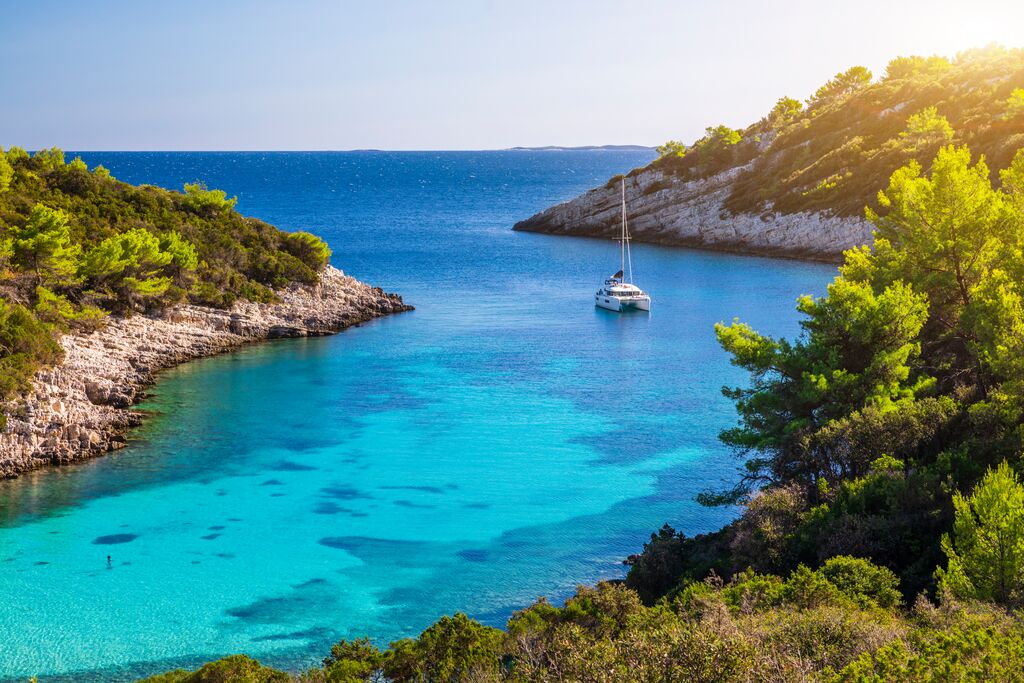 A beautiful bay in Croatia, with pale blue water and a boat gently sailing away on calm waters