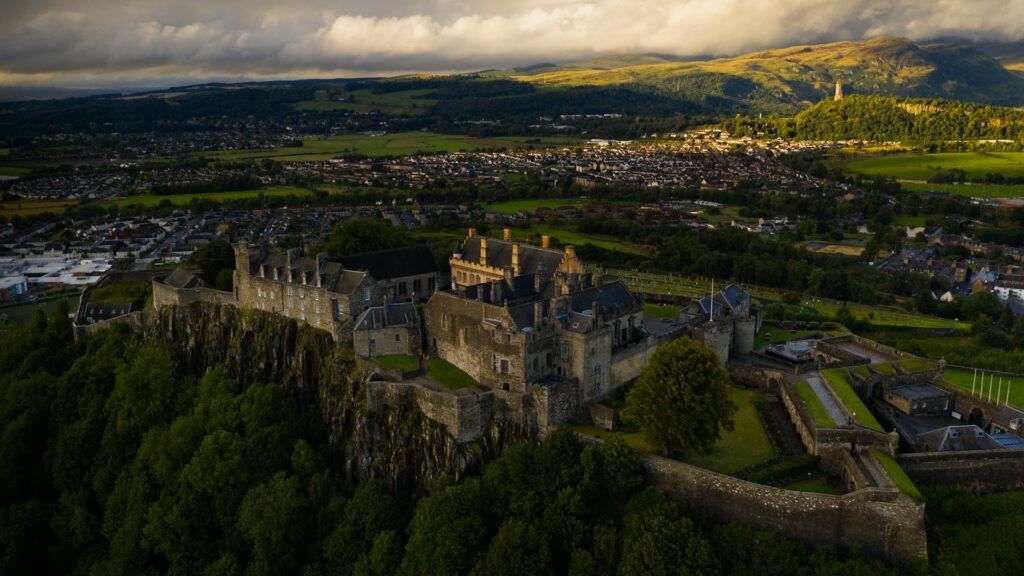 Stirling castle photographed from the air, with sunlit hills and low clouds in the background