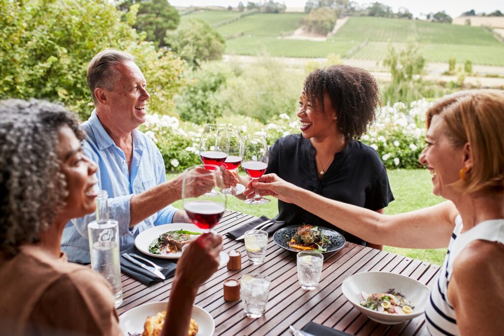 A group of older travellers toast their friendship over lunch overlooking green gardens and vineyards