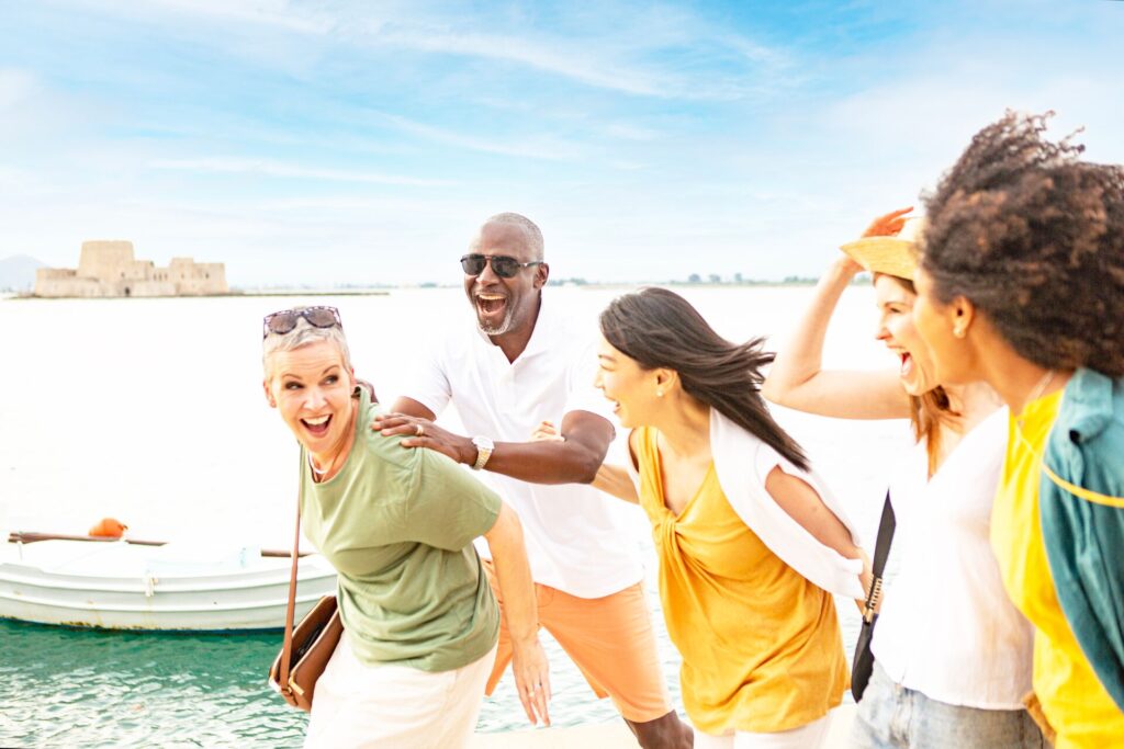 A group of senior travellers smile and joke with the sea behind them.