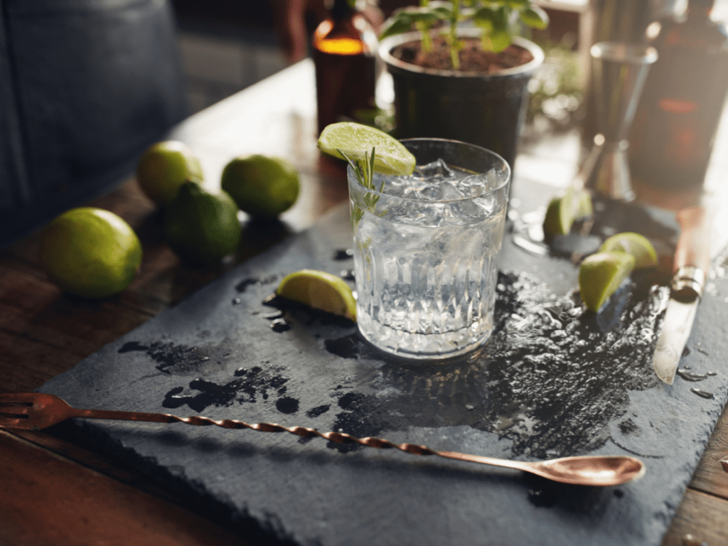 A glass filled with a Gin cocktail with a garnish of Lime and rosemary