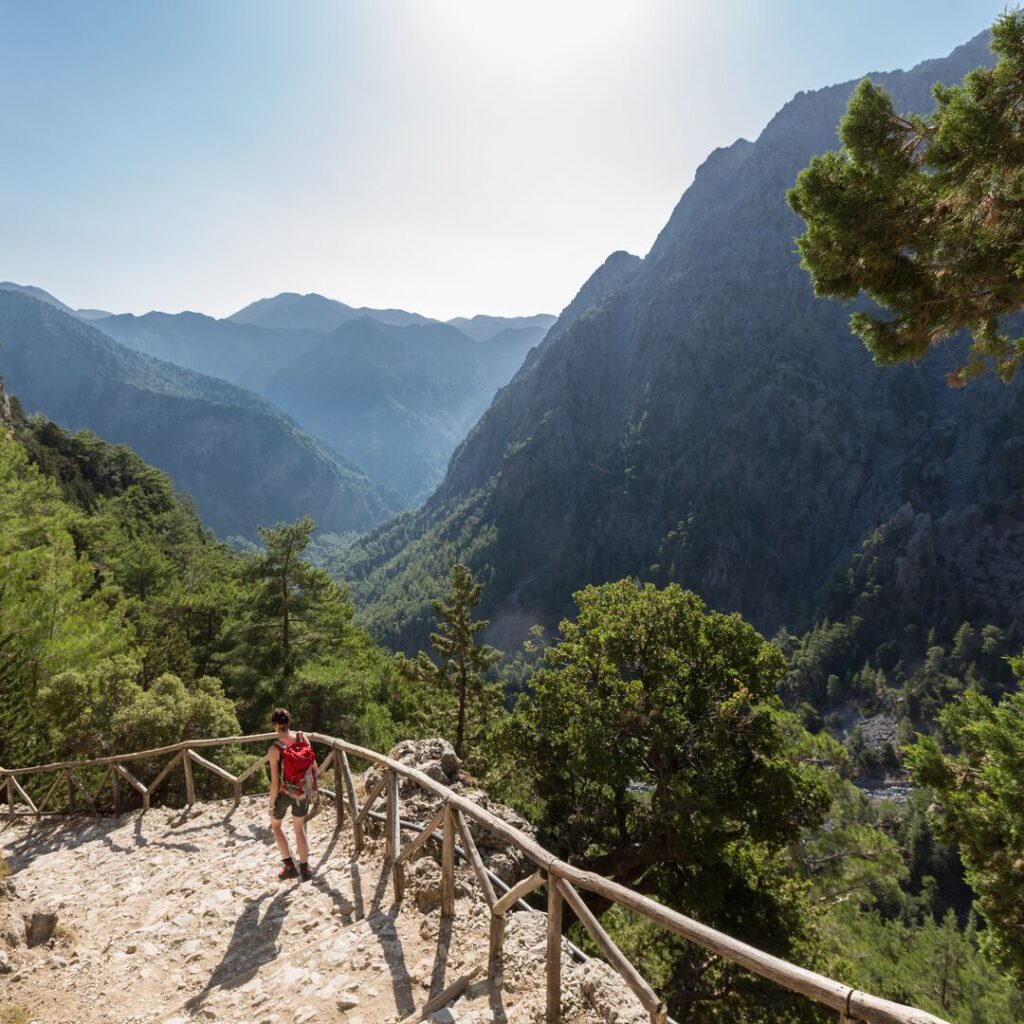 Mountains in Greece, with a little path weaving down to ground. A woman is walking down this path.