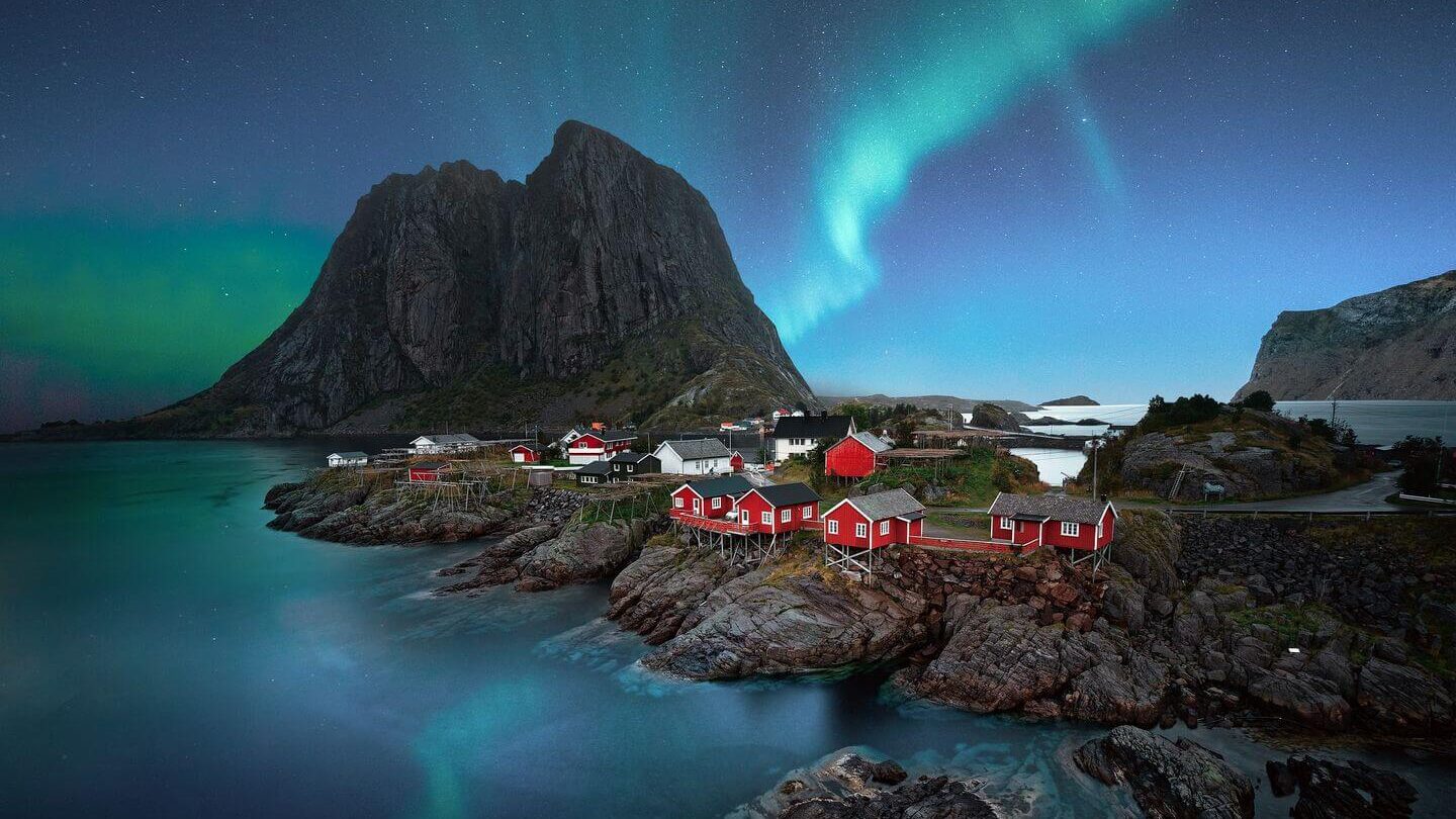 red cottages Northern Lights over rocky coastline Norway