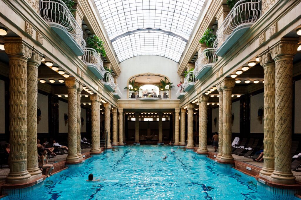 Ornate indoor swimming pool under a glass ceiling, with stone pillars surrounding it