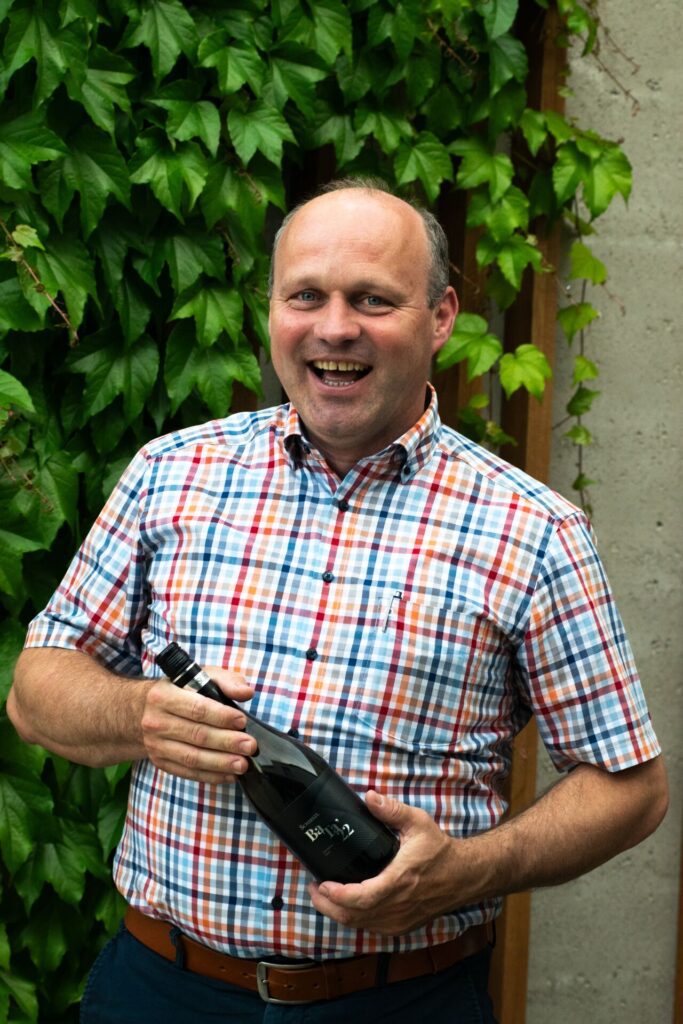The owner and head of the Schieszl family restaurant, holding a bottle of wine in front of a backdrop of leaves