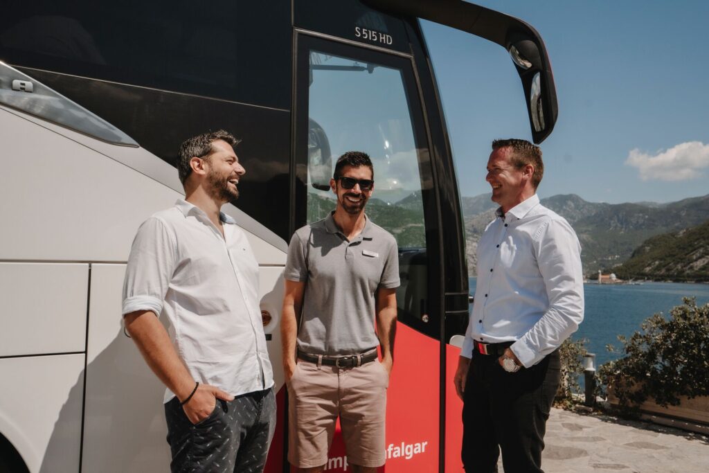 A driver, Travel director and Local Expert laughing in front of a Trafalgar coach - three staff members to whom tipping is customary