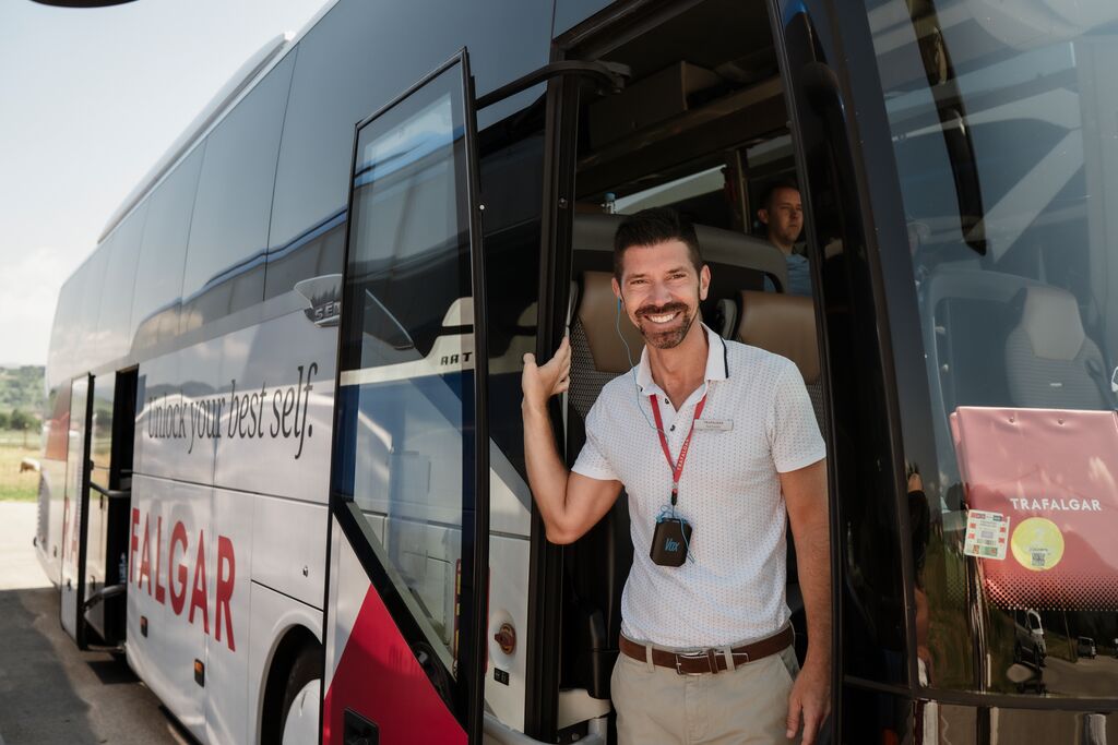 A man wearing a red lanyard stands looking out of the door of a coach