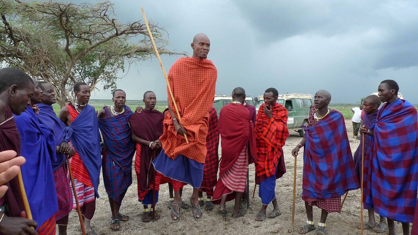 Group of Maasai men clad in traditional shuka garments, an essential element of what to wear in Tanzania, gathered outdoors under a cloudy sky.