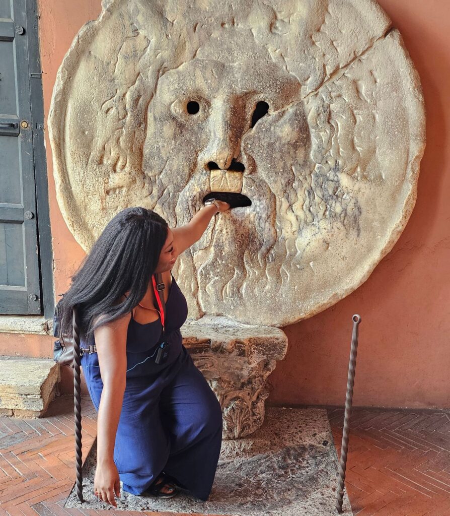 Image of TUA entrant Ariel putting her hand into 'the Mouth of Truth' monument in Rome