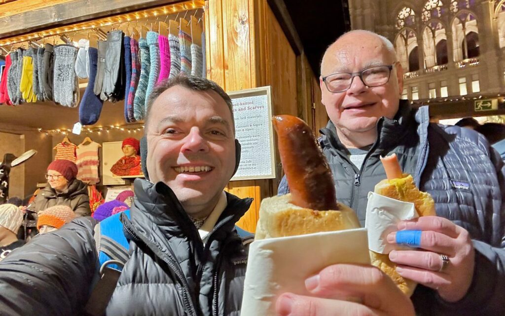 Selfie photo of Jason with his partner holding hotdogs at a European Christmas market