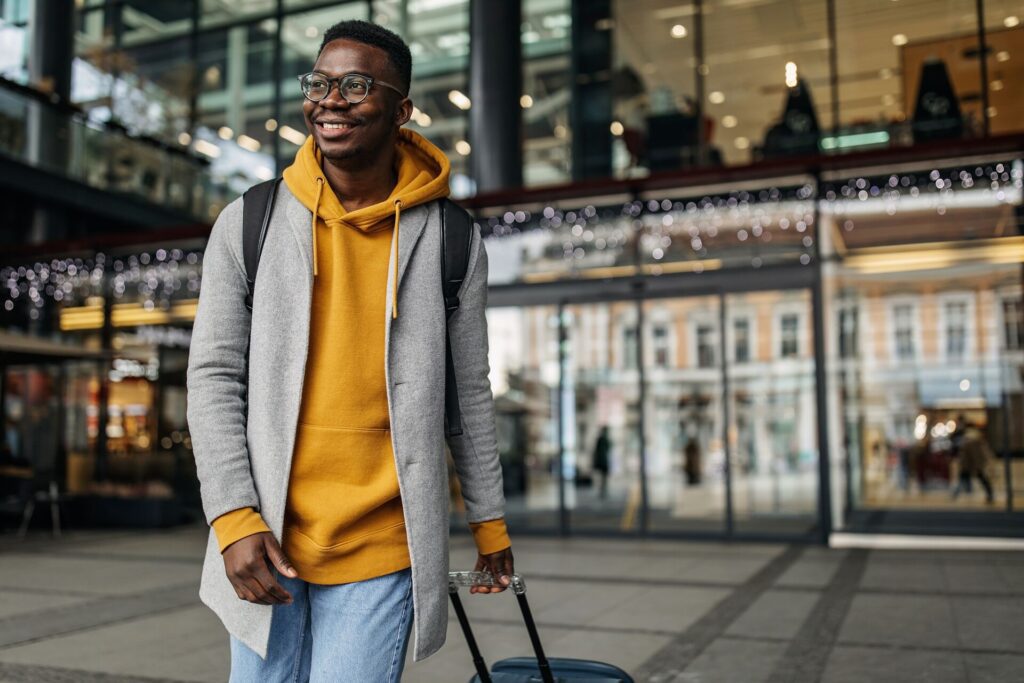 Guy walking from airport dragging his suitcase and smiling.