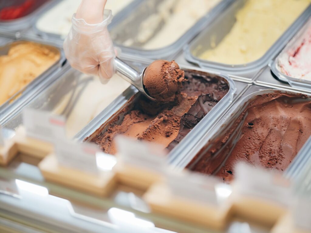 A hand scooping a chocolate gelato in a cafe.