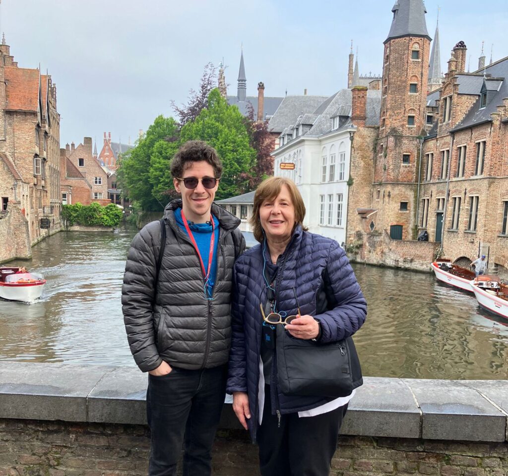 Nolan and his mother standing on a bridge overlooking a river with old buildings either side