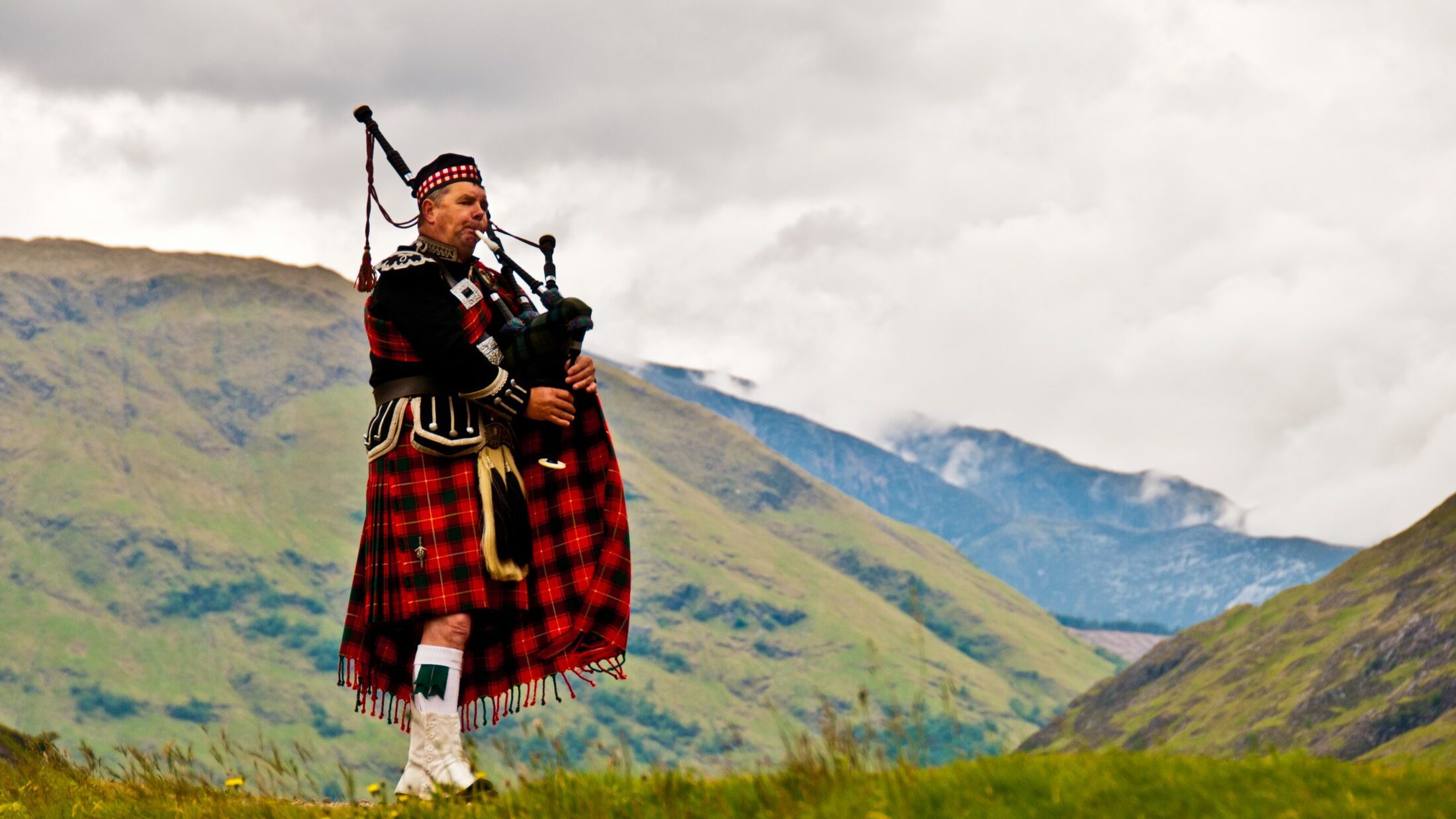 Visit Scotland in 2020 to see a man in a kilt playing bagpipes amidst the stunning mountains.