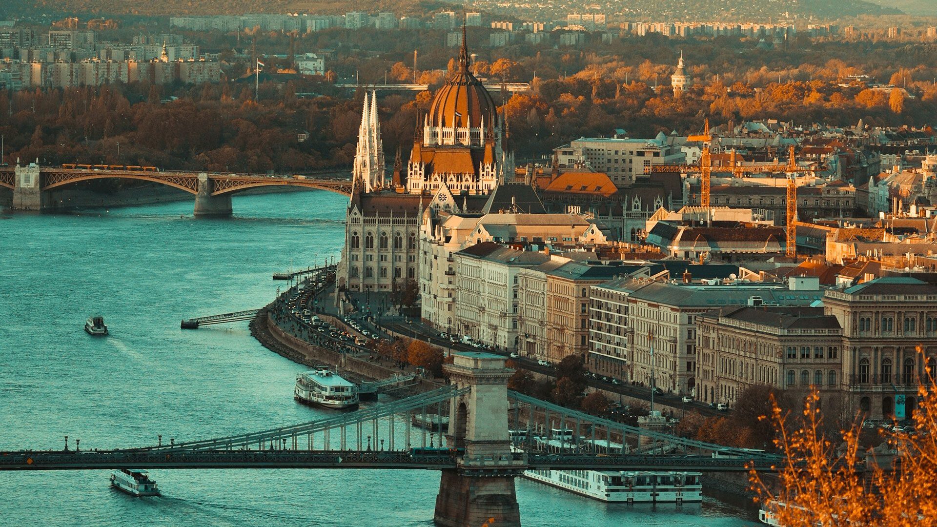 Aerial view of the Danube River through the centre of Budapest, with wooded hills and apartment blocks in the distance