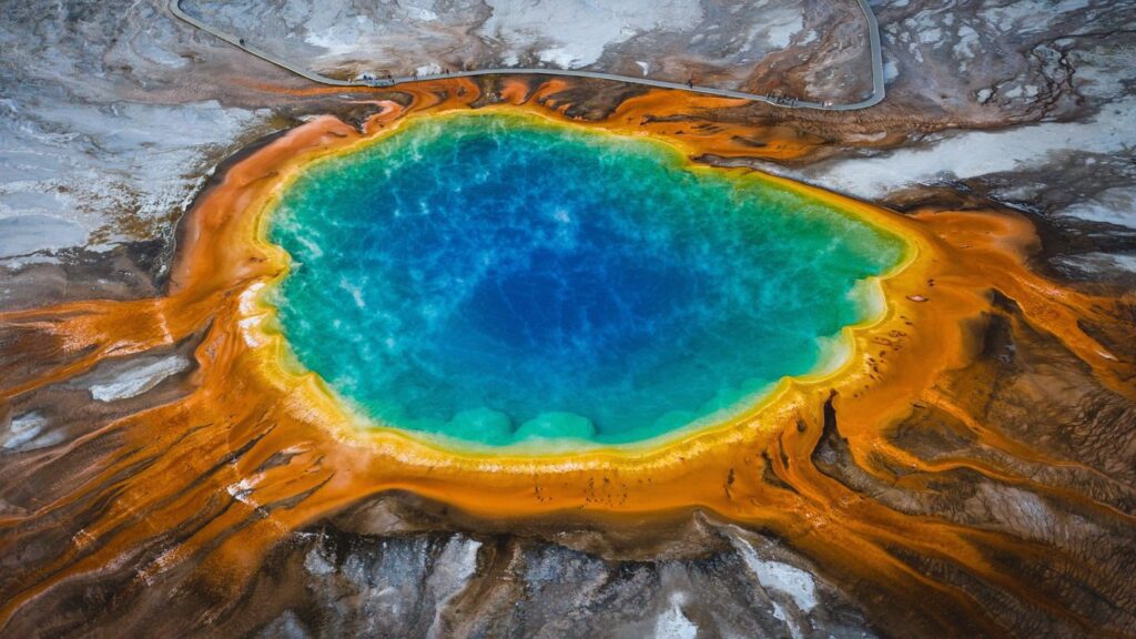 Aerial view of the grand prismatic spring in Yellowstone National Park, showing vibrant blue water surrounded by orange microbial mats.