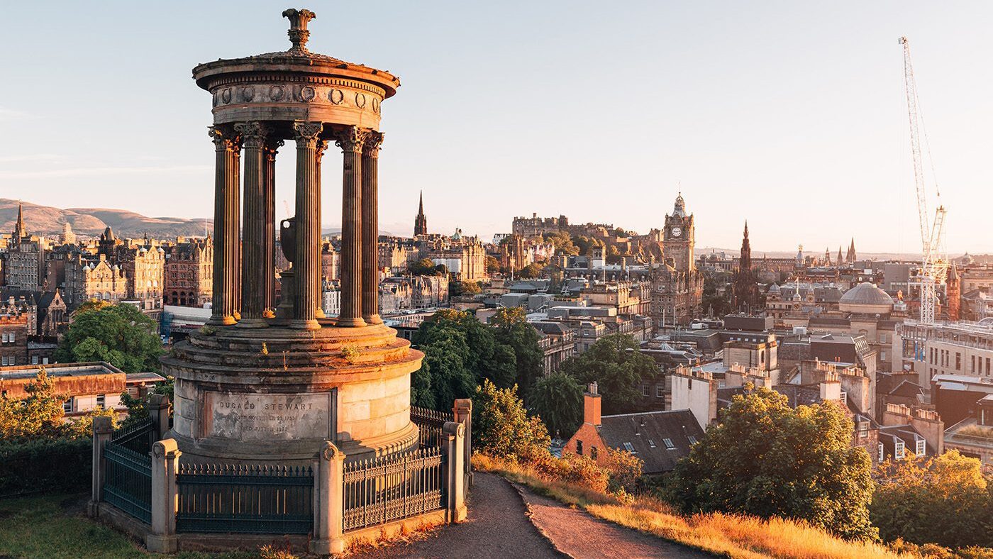 Sunset view of Edinburgh with the Dugald Stewart Monument in the foreground overlooking the cityscape while travelling to Scotland in September.