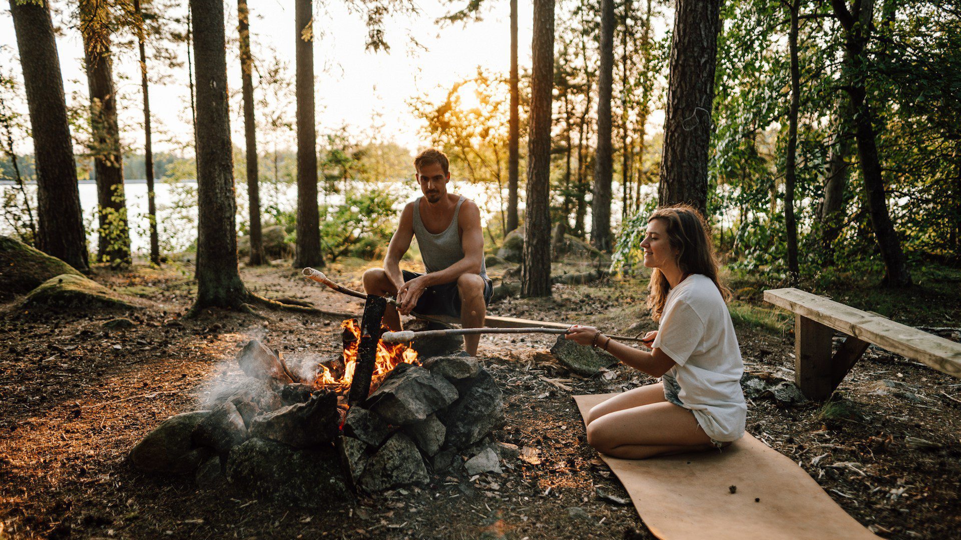 A young couple cooking on sticks over a campfire in the woods