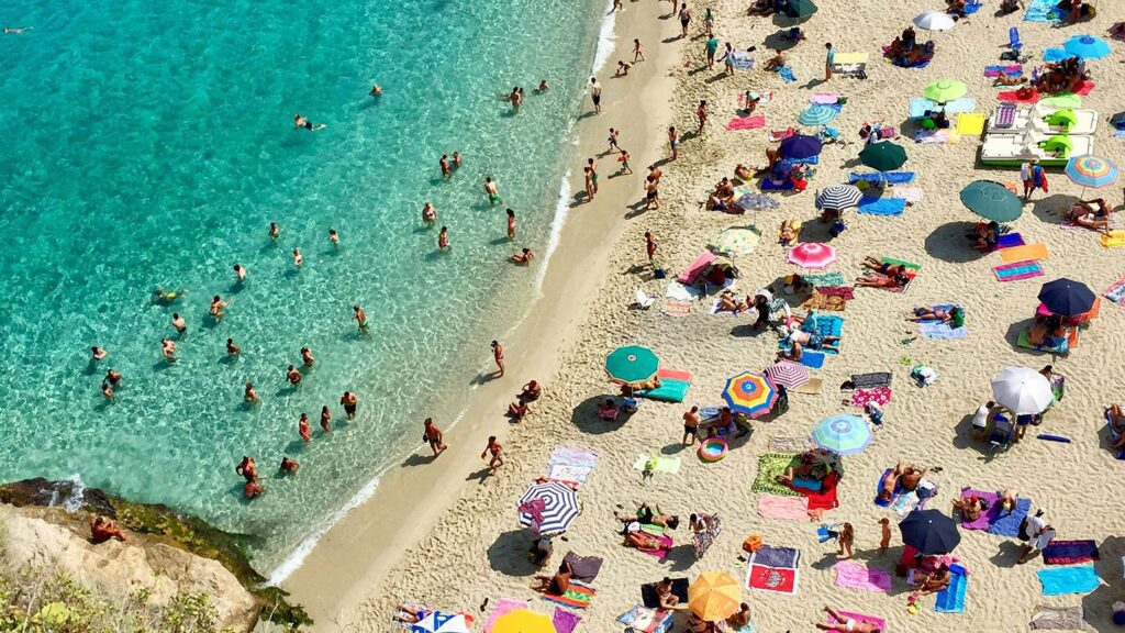 A beach with blue water and colorful sun umbrellas