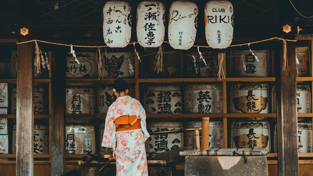 A woman in a kimono views a display of sake barrels and hanging lanterns at a traditional Japanese setting, highlighting unique things to do in Japan.