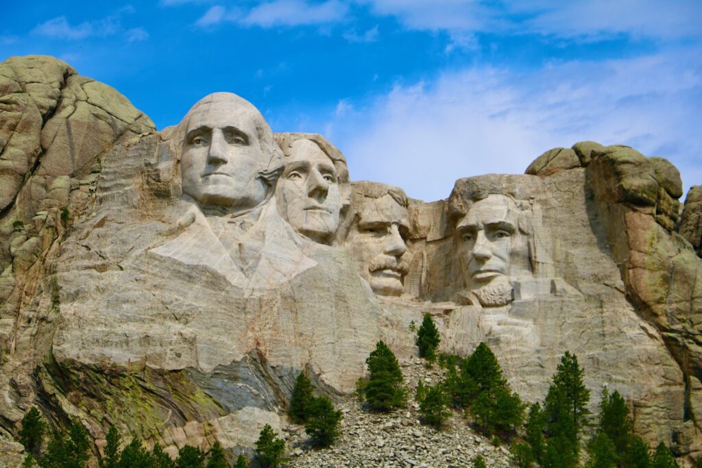 Sculptures of four U.S. presidents carved into Mount Rushmore National Park under a blue sky with light clouds, ideal for national park vacations for families.