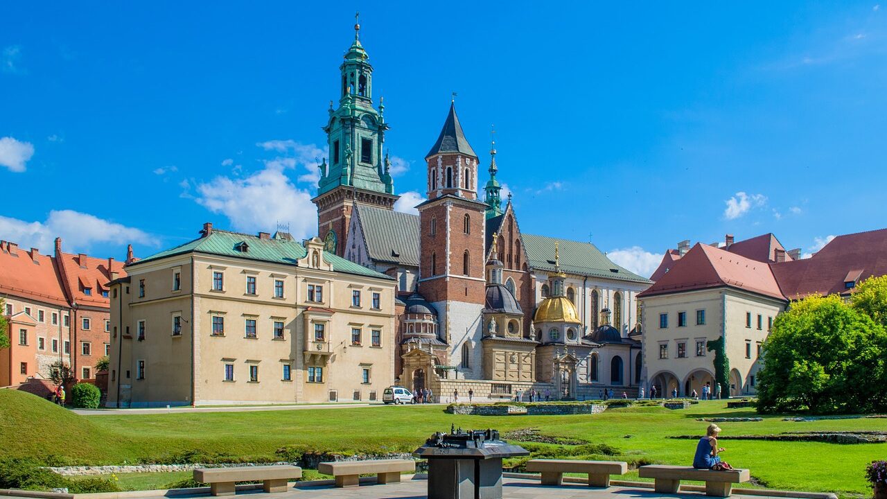 Guide to Wawel royal castle complex with green lawns and clear blue skies in Krakow, Poland.