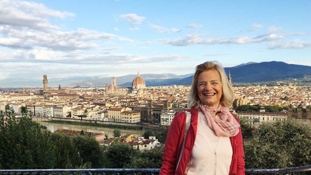 A woman smiling at the camera with Florence's heritage cityscape, including the cathedral and river, in the background.