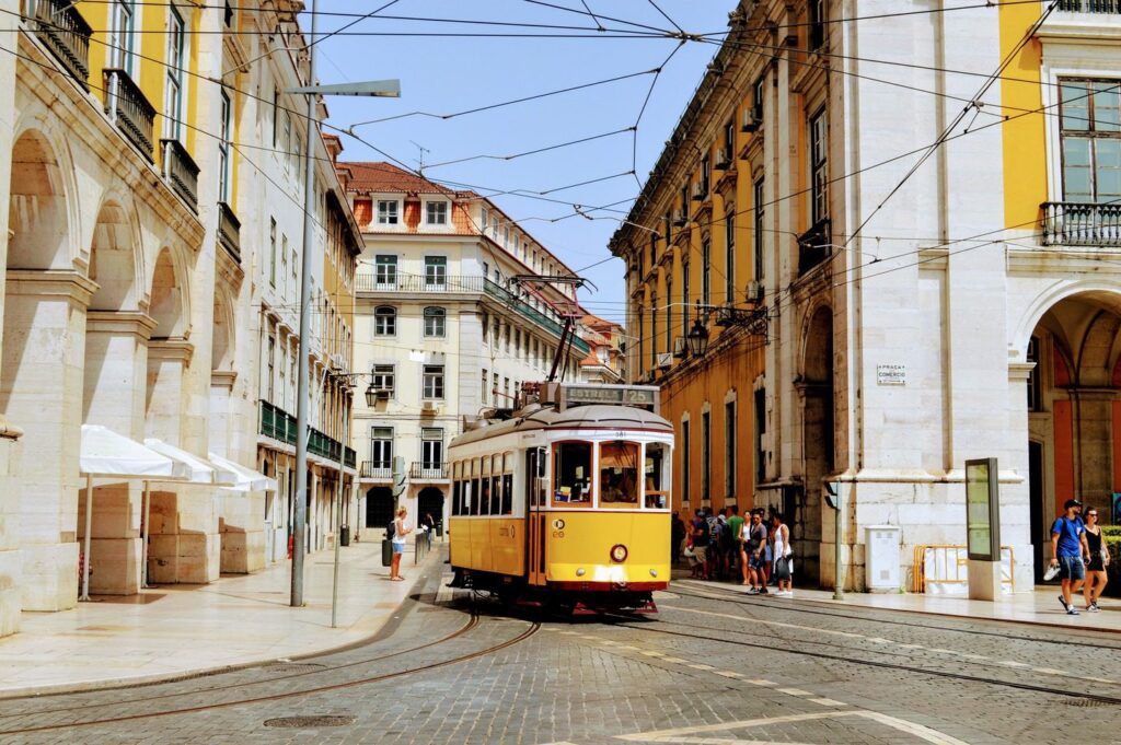 A vintage yellow tram travels through a bustling street lined with classical architecture in a sunny, European city during spring tours.