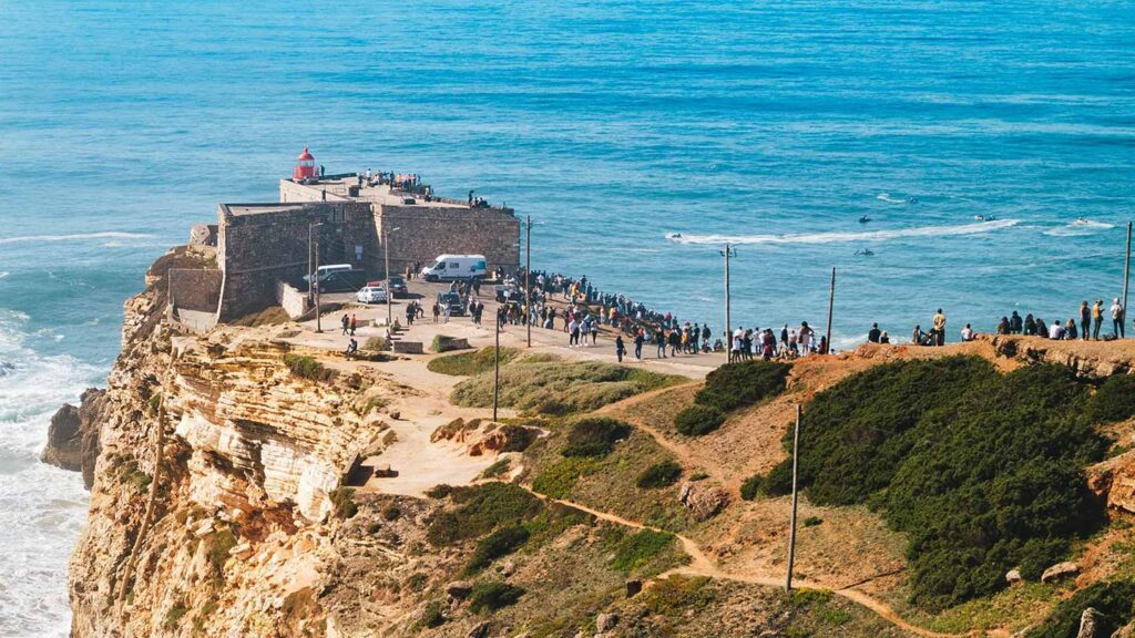 Lighthouse overlooking a cliff in Portugal with visitors enjoying the scenic coastal view.