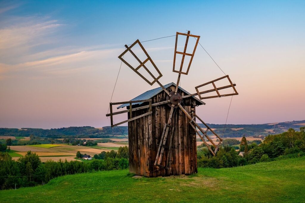 Traditional wooden windmill on a hillside in Poland, overlooking the scenic rural countryside at sunset.