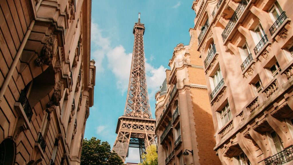 The Eiffel Tower viewed between traditional Parisian buildings under a clear blue sky during spring tours.