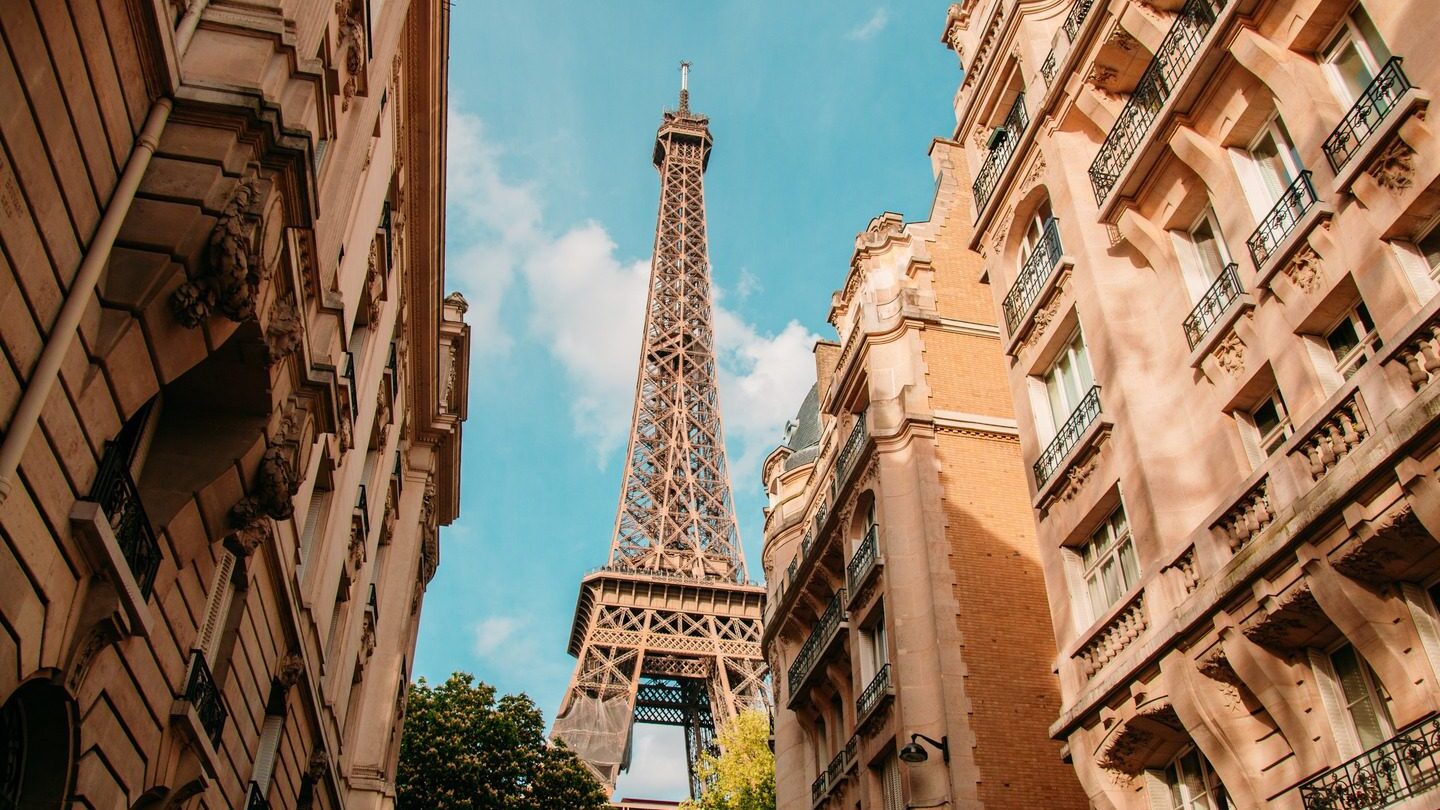 The Eiffel Tower viewed between traditional Parisian buildings under a clear blue sky during spring tours.
